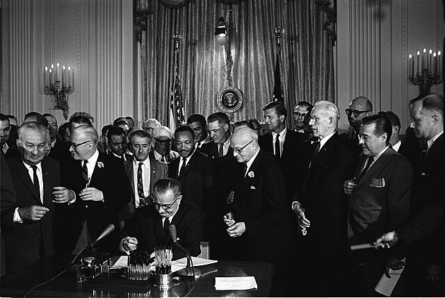 King standing behind President Johnson as he signs the Civil Rights Act of 1964
