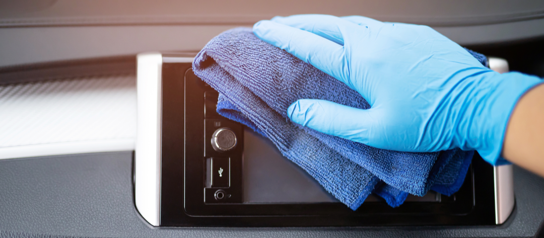 gloved hand cleans a car touch screen with microfiber cloth